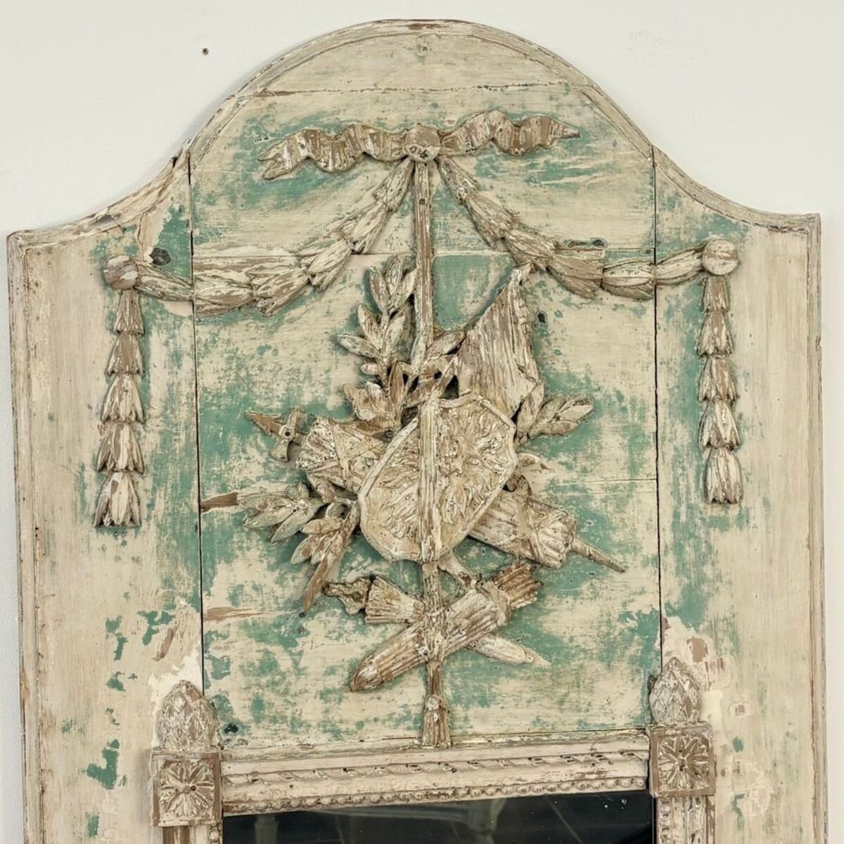Superb small Louis XVI period trumeau mirror in carved wood decorated with warrior attributes, originally painted. - JAA